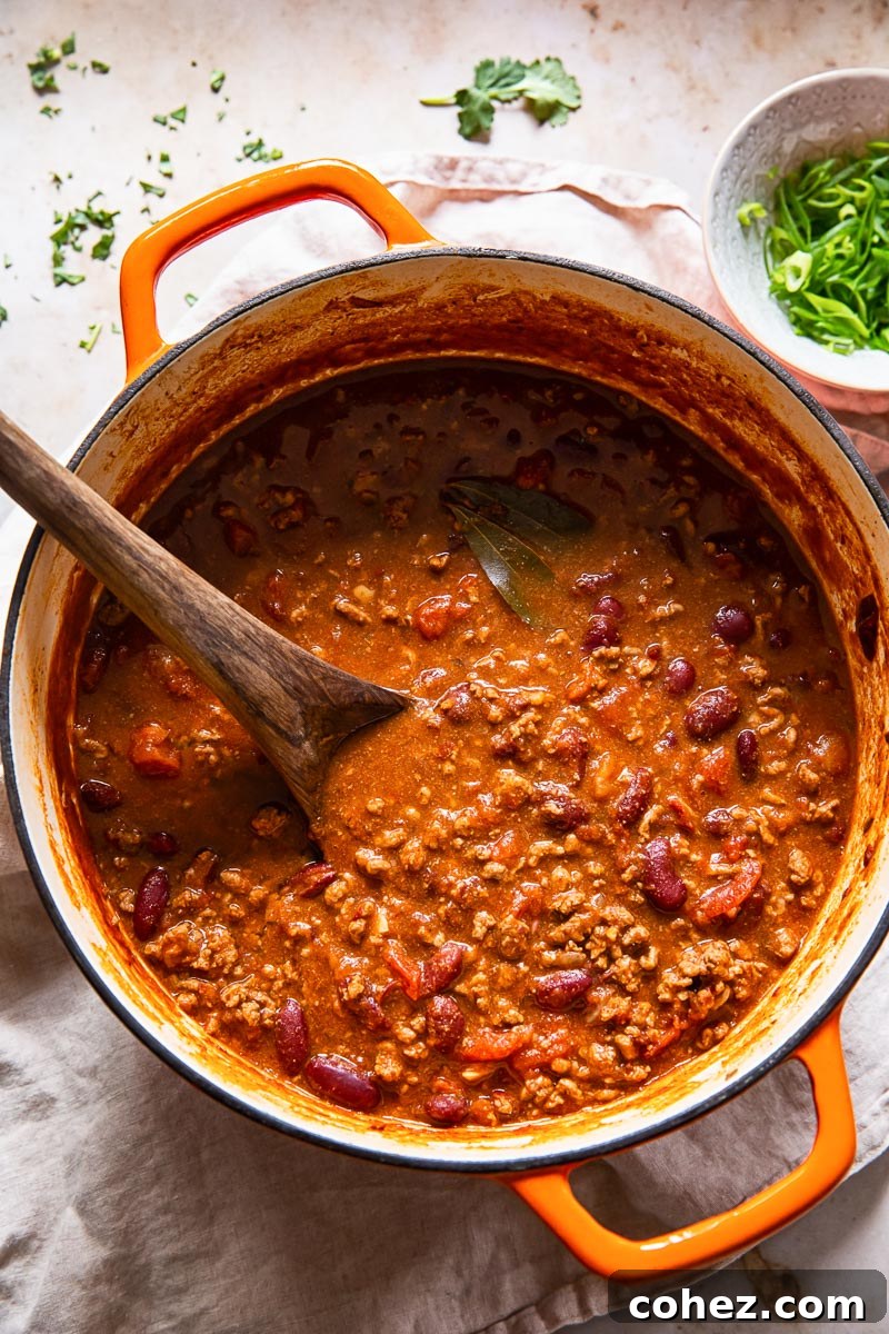 Top-down view of a vibrant beef and kidney bean chili con carne simmering in a rustic orange Dutch oven, showcasing its rich texture.