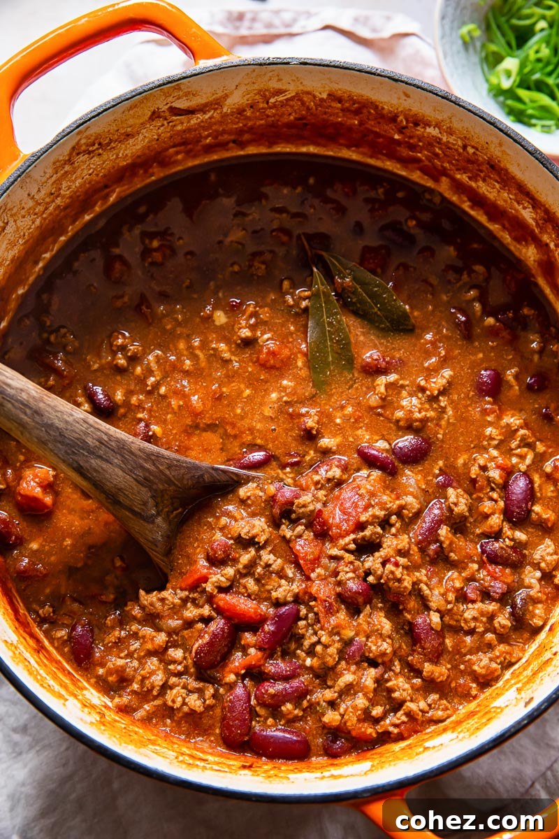 Hearty chili con carne with kidney beans, simmering in a rustic orange Dutch oven, ready to be served.