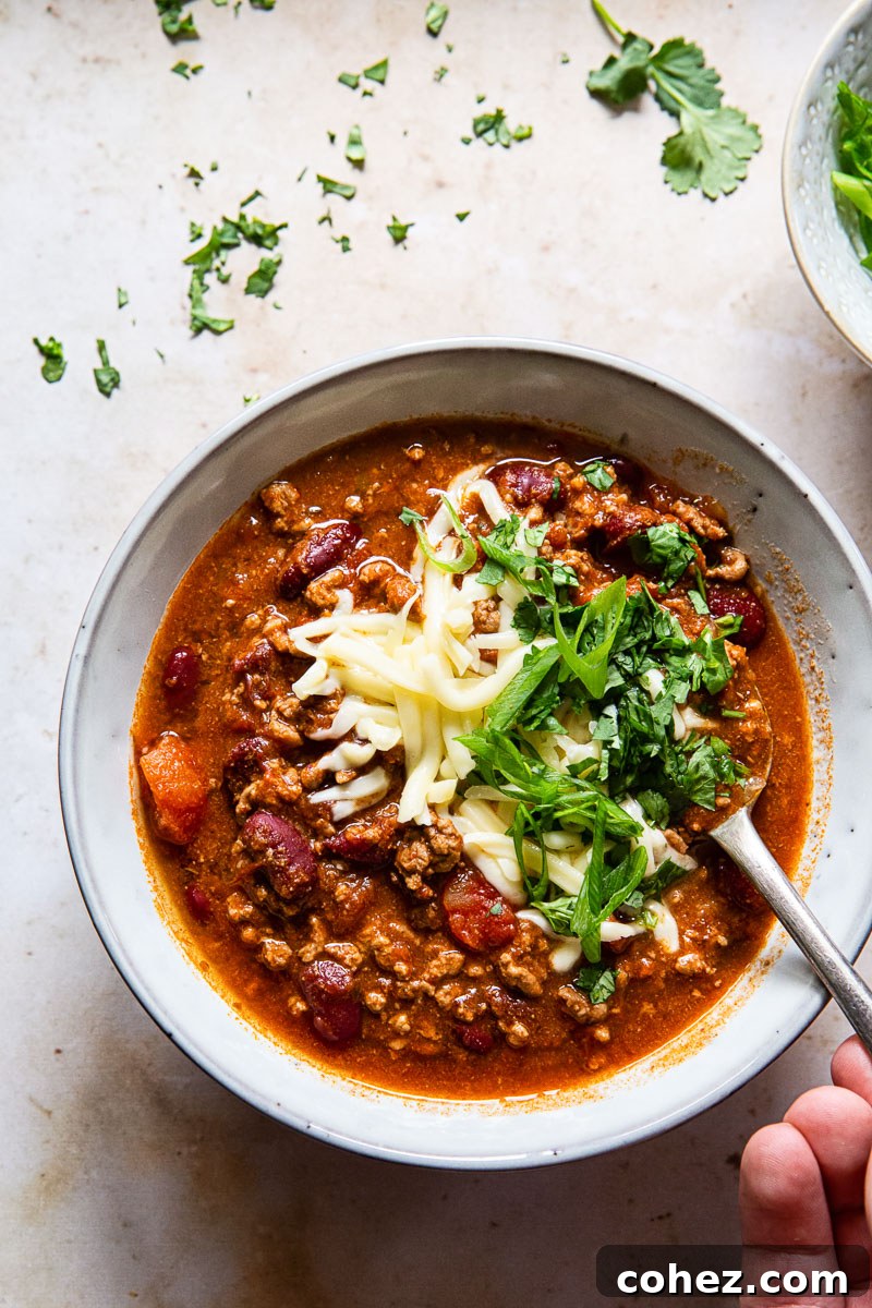 A hand holding a spoon dipped into a bowl of rich, homemade chili, showcasing its inviting texture and warmth.