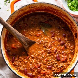 Top-down view of a vibrant beef and kidney bean chili con carne simmering in a rustic orange Dutch oven, showcasing its rich texture.