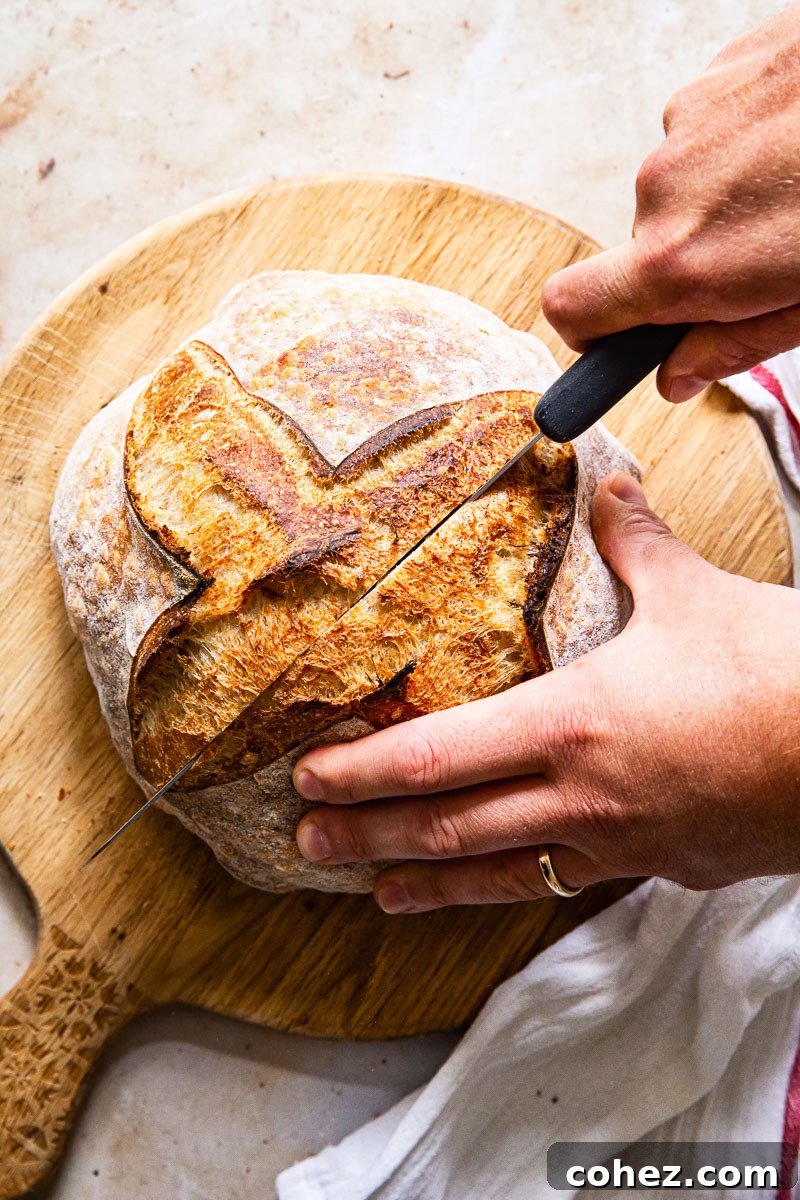 Top-down view of a freshly baked sourdough bread being sliced on a wooden board, revealing its interior crumb.