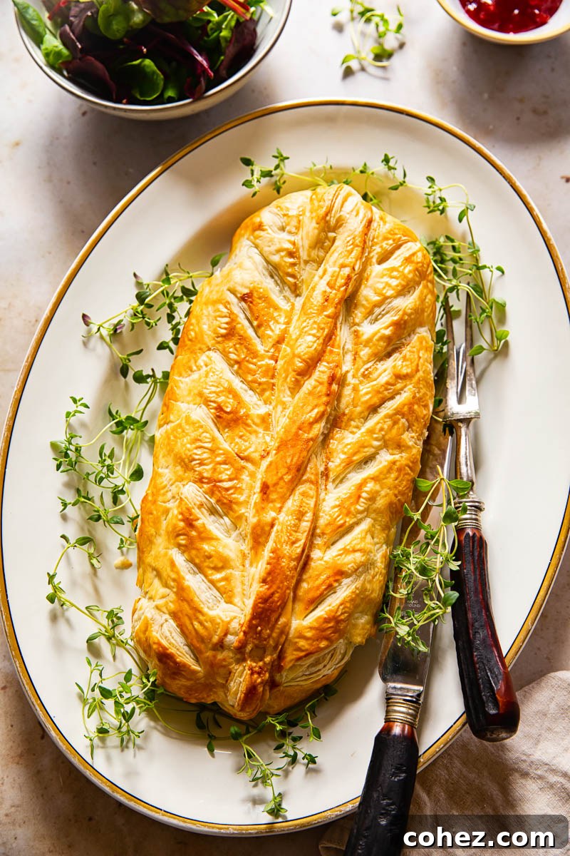 Vegetarian Wellington served on a white platter, accompanied by a fresh salad and a bowl of cranberry sauce