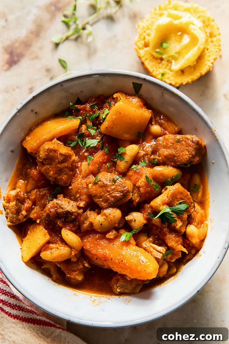 Hearty slow cooker pork stew with carrots and butternut squash in a rustic grey bowl, perfect for cold weather comfort.