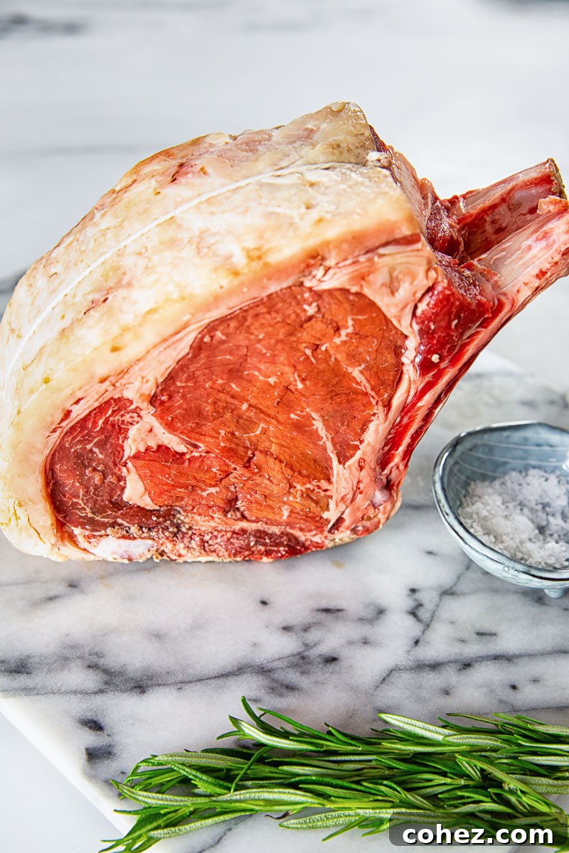 An uncooked rib of beef, generously coated with the honey mustard rub, rests on a pristine marble surface, ready for roasting.