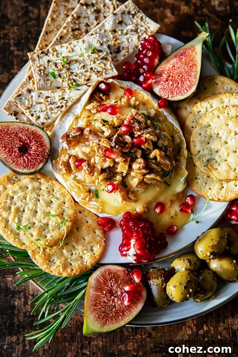 A wheel of brie cheese artfully topped with walnuts and vibrant pomegranate seeds, elegantly surrounded by a selection of crackers, fresh figs, and olives on a rustic serving platter.