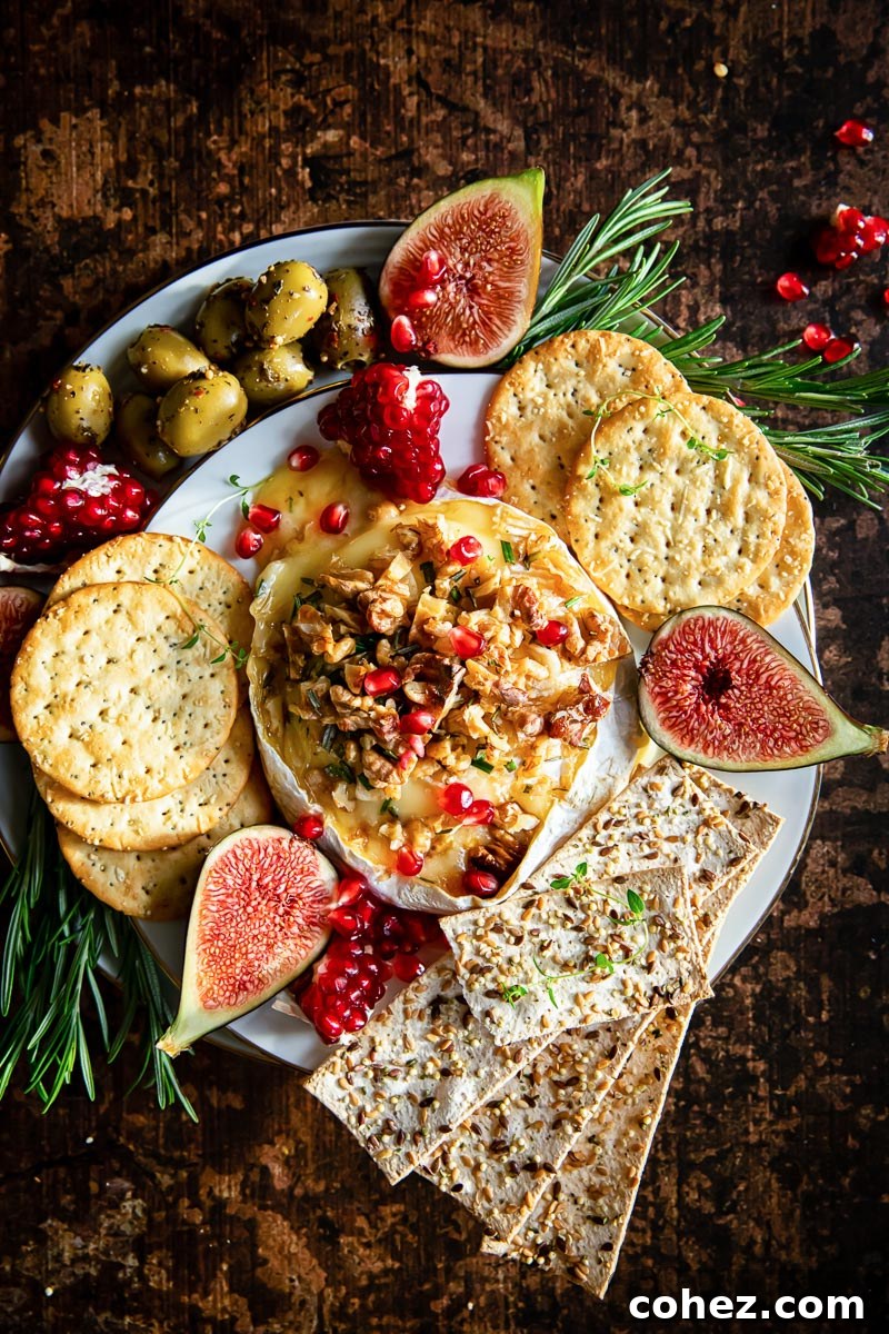 A top-down view of a gloriously baked brie, generously topped with walnuts and pomegranate seeds, elegantly surrounded by a festive array of crackers, vibrant olives, and fresh figs on a serving board.