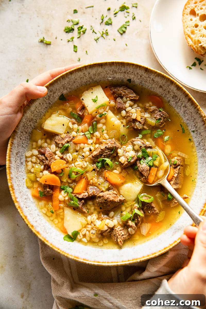 A comforting bowl filled with tender beef, hearty vegetables, and plump barley soup, held warmly in hands with a spoon ready to enjoy.