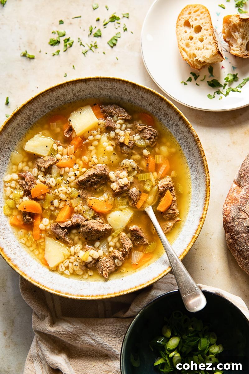Hearty Beef and Barley Soup 5 top down view of a bowl of soup with a spoon, a plate with slices of bread and a black bowl with chopped herbs