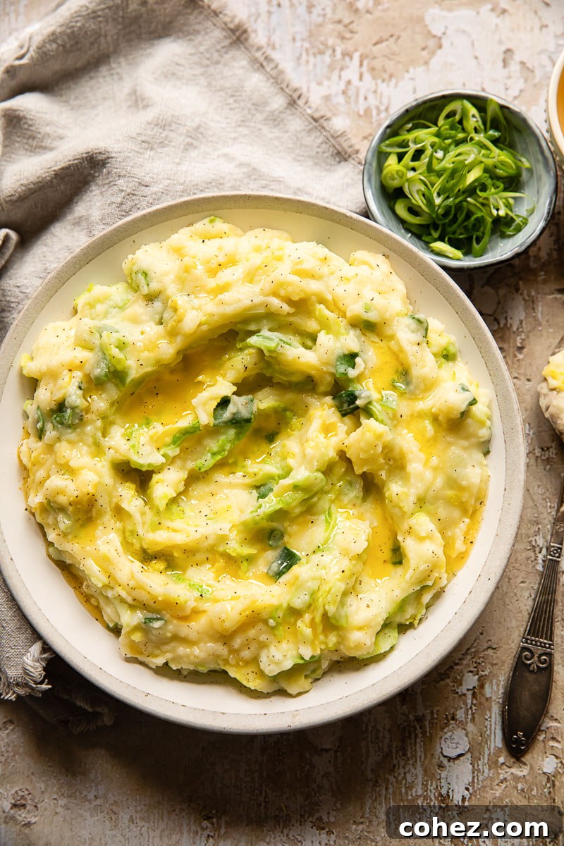 Top-down view of Irish Colcannon in a rustic bowl, with a small dish of sliced green onions nearby and a grey napkin
