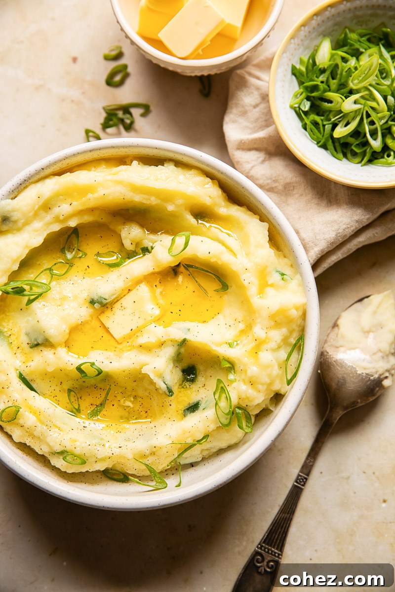 top down view of Irish Champ topped with melted butter, a spoon and a bowl with green onions and cubed butter next to it.