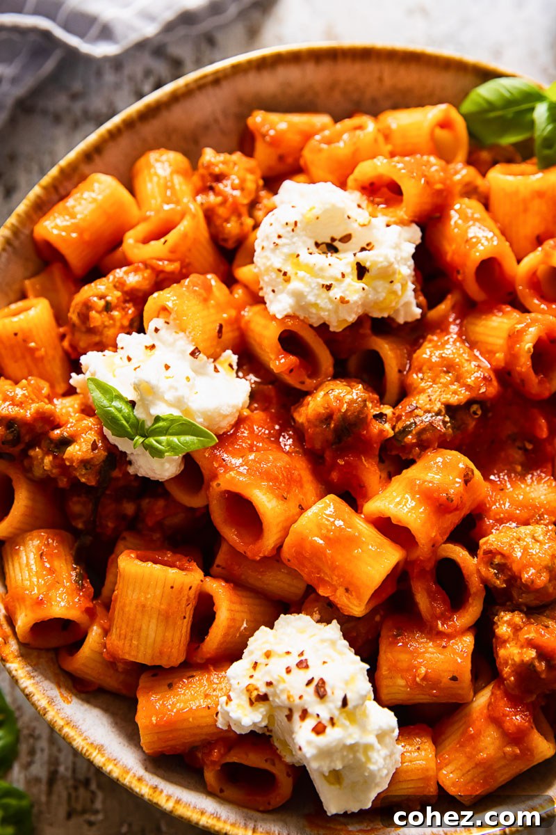 Top-down view of rigatoni pasta with spicy sausage in a rich tomato sauce, generously topped with creamy ricotta cheese and fresh basil