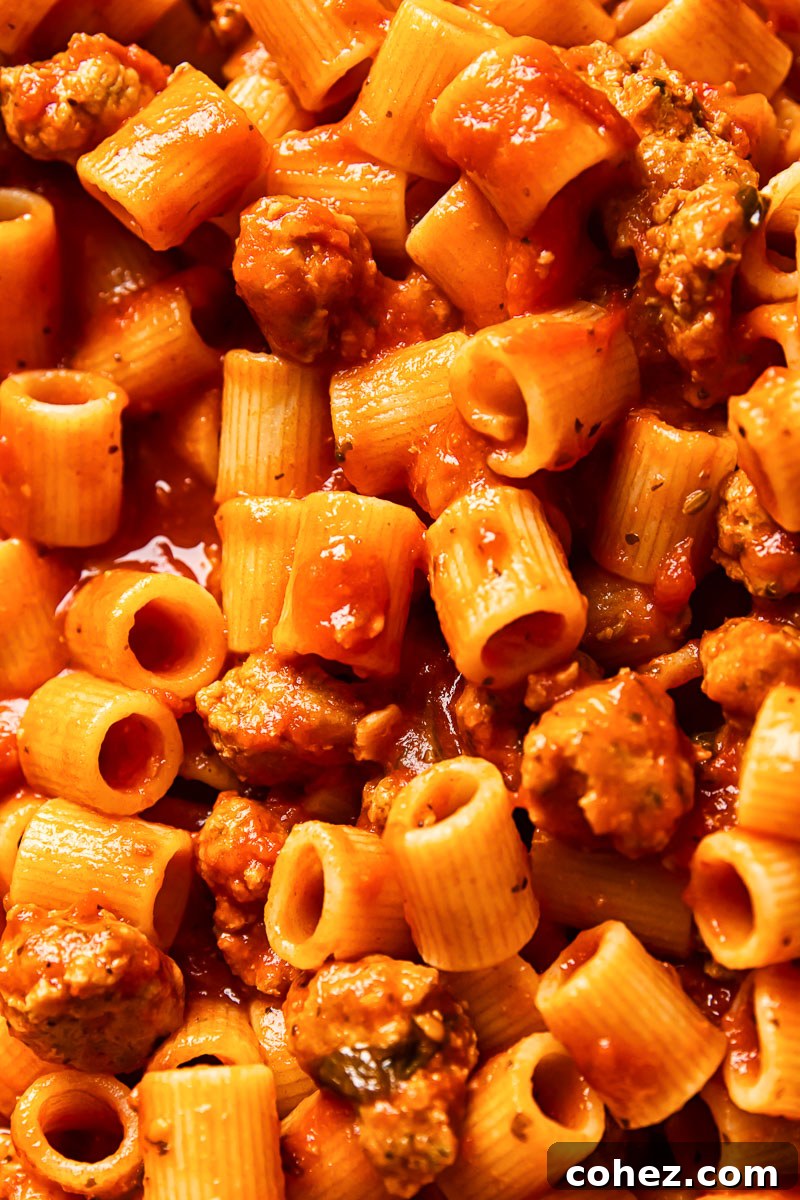 Close-up of a serving of spicy sausage pasta with ricotta and fresh basil, ready to eat