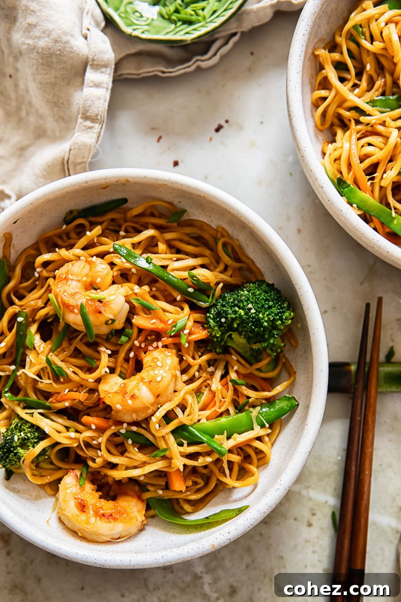 shrimp chow mein in a decorative bowl, accompanied by chopsticks and a cream-colored napkin