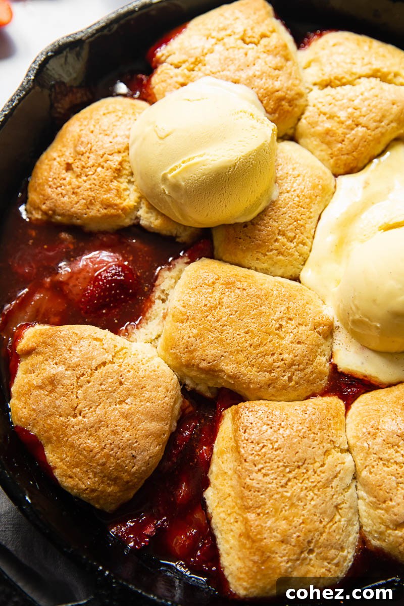 Top-down view of a golden-baked strawberry cobbler in a dish, topped with a melting scoop of vanilla ice cream.