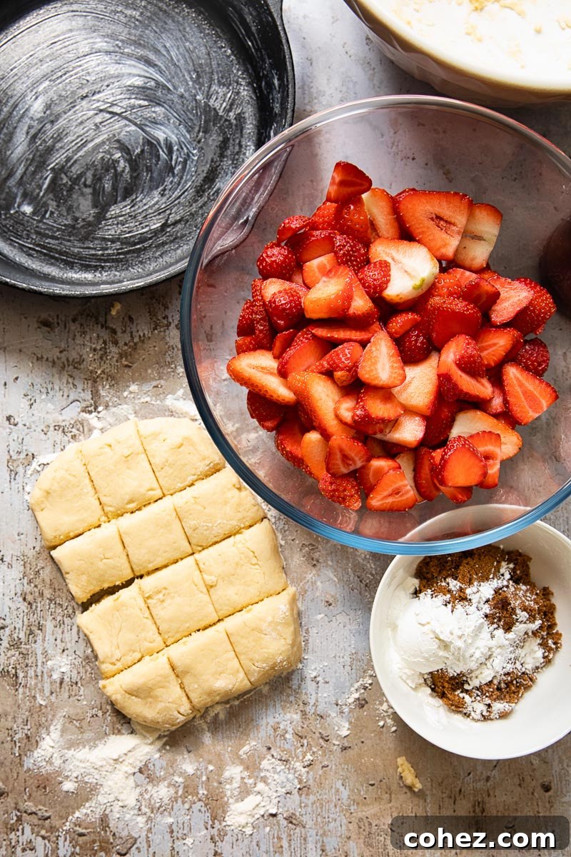 A top-down view of fresh ingredients for a strawberry cobbler, including sliced strawberries, butter, flour, and sugar, laid out on a wooden surface.