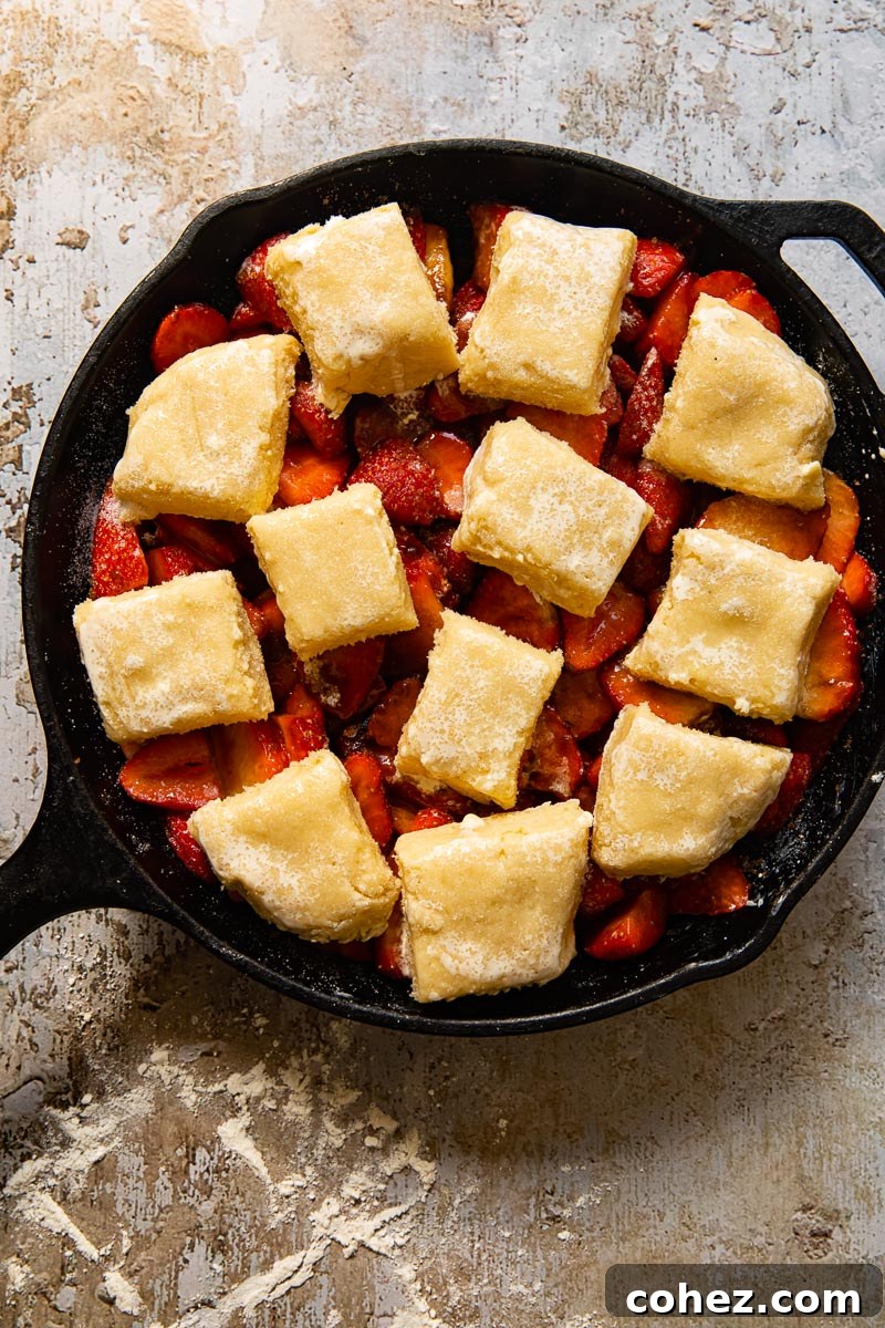 An unbaked strawberry cobbler in a baking dish, with raw biscuit topping arranged over the sliced strawberries, ready for the oven.