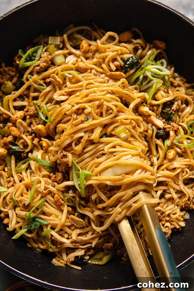 Close-up of freshly prepared Sichuan Dan Dan noodles in a black wok, with tongs lifting some noodles