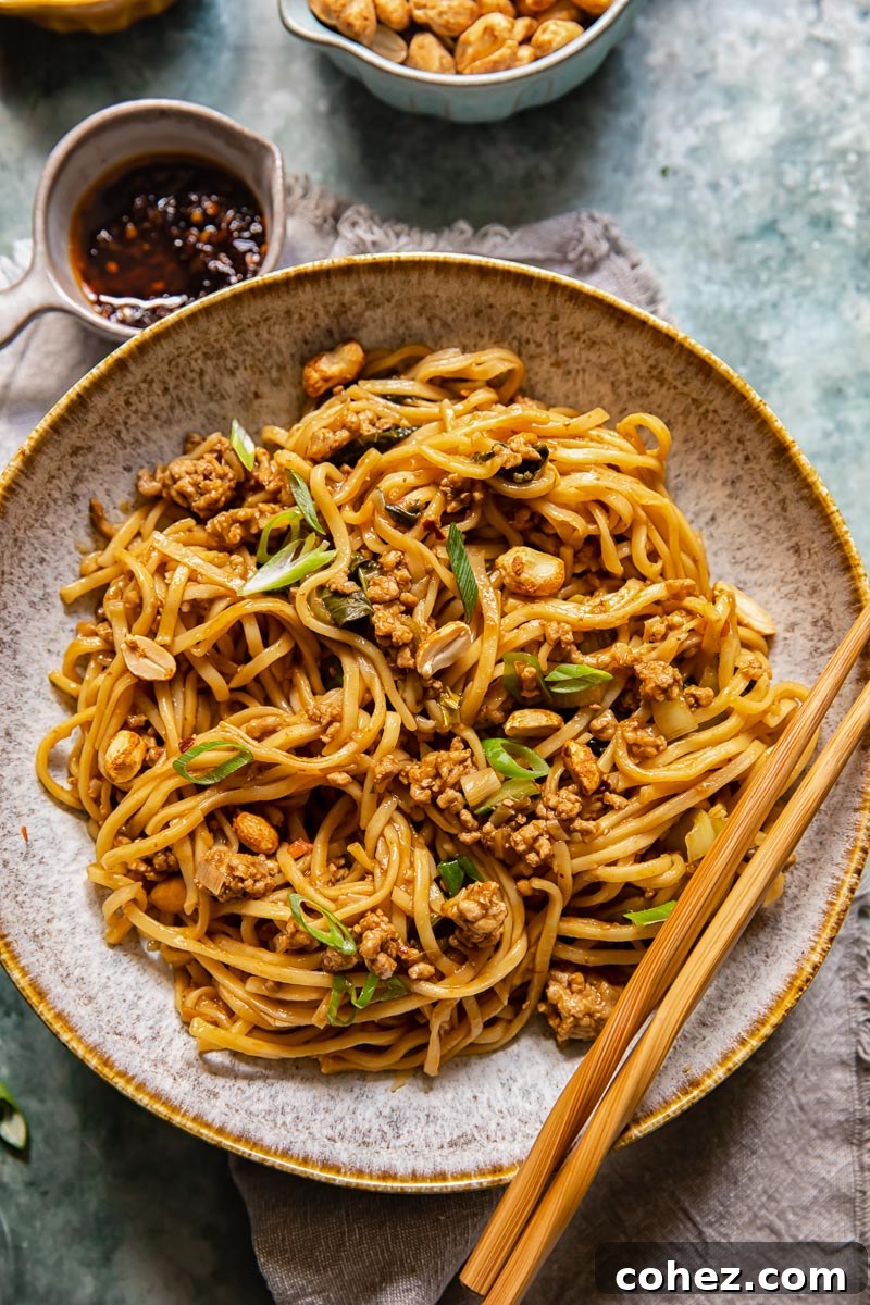 A bowl of vibrant Dan Dan noodles topped with ground pork, green onions, and peanuts, with chopsticks resting on the rim