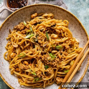A bowl of vibrant Dan Dan noodles topped with ground pork, green onions, and peanuts, with chopsticks resting on the rim