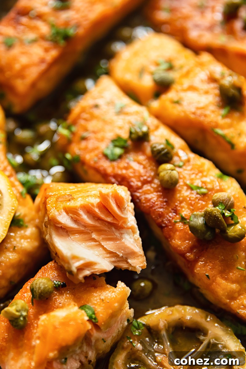 Close-up view of a perfectly cooked salmon fillet, richly coated in a lemon caper sauce and garnished with fresh parsley.