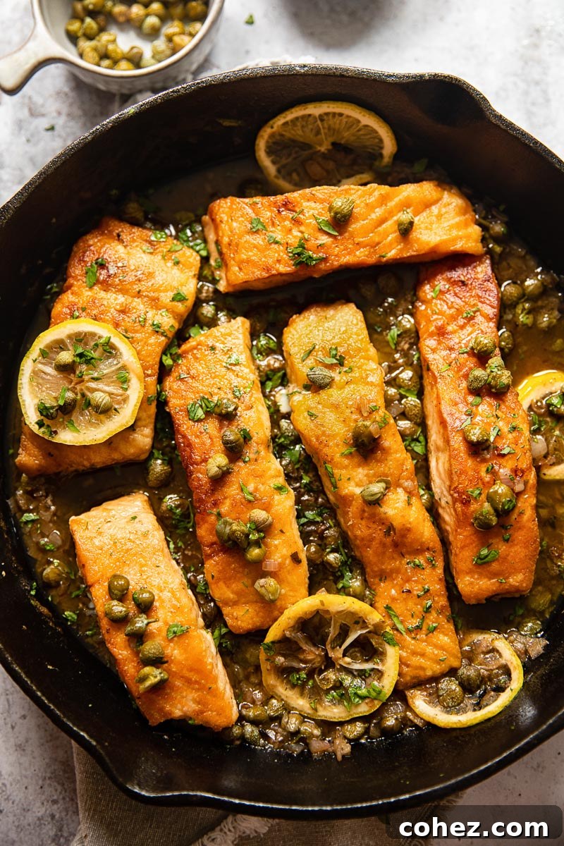 Top-down view of cooked salmon piccata, generously covered in lemon-caper sauce, garnished with fresh parsley.