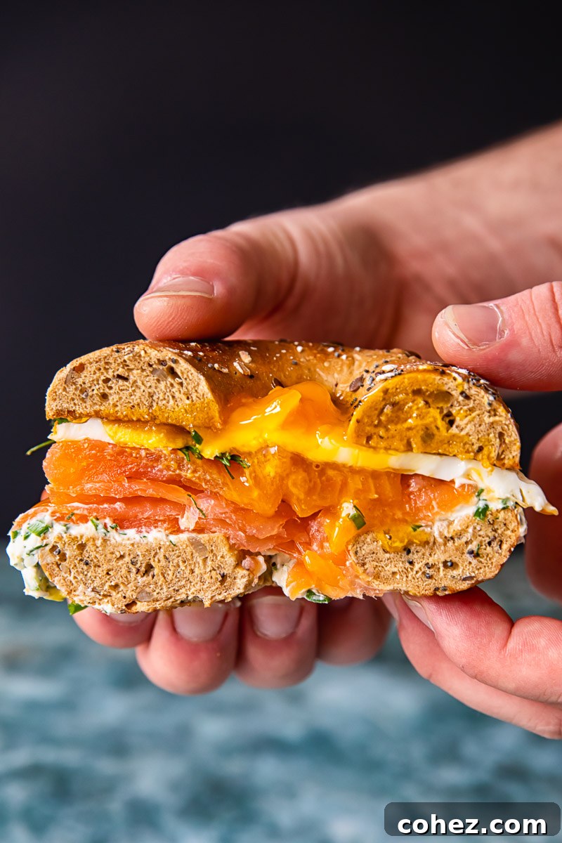 Cross-section of a perfectly assembled breakfast bagel sandwich, showcasing layers of herbed cream cheese, smoked salmon, and a runny fried egg