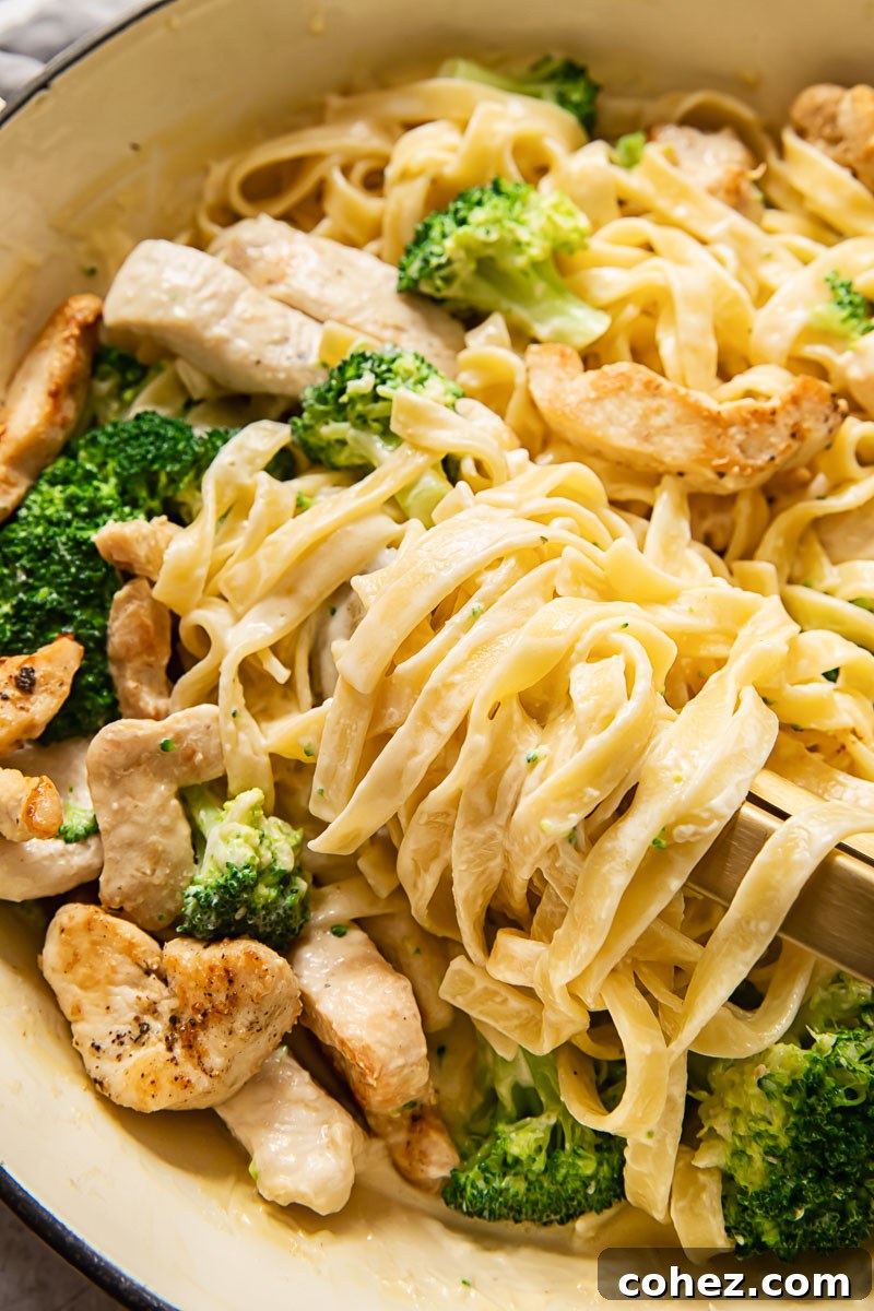 Close-up shot of creamy fettuccine with chicken and broccoli simmering in a large pan, ready to be served.
