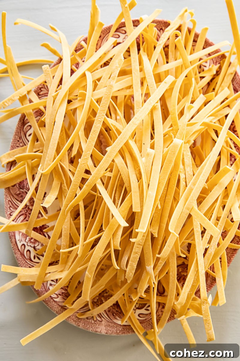 Soul-Warming Chicken Noodle Soup 3 A generous pile of freshly made, hand-cut noodles resting on a white platter, ready to be added to a homemade chicken noodle soup.