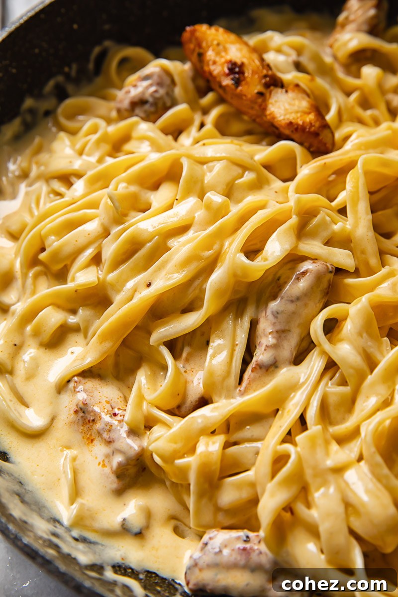 A large pan filled with fettuccine pasta, tender Cajun chicken, and creamy Alfredo sauce, garnished and ready to serve.