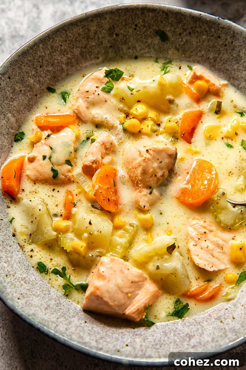 A close-up shot of creamy salmon chowder in a grey bowl, highlighting the chunks of salmon, corn, and potatoes.