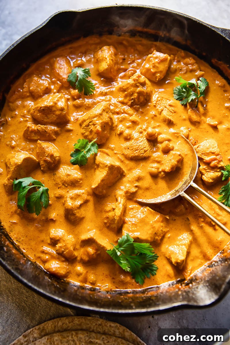 Golden Chicken in a Silken Masala 2 Top-down view of creamy Chicken Tikka Masala simmering in a large, rustic pan, garnished with fresh cilantro.