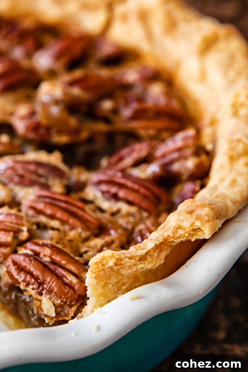 A close-up view of the golden-brown, beautifully crimped edge of a pecan pie, emphasizing its perfectly flaky and buttery crust.