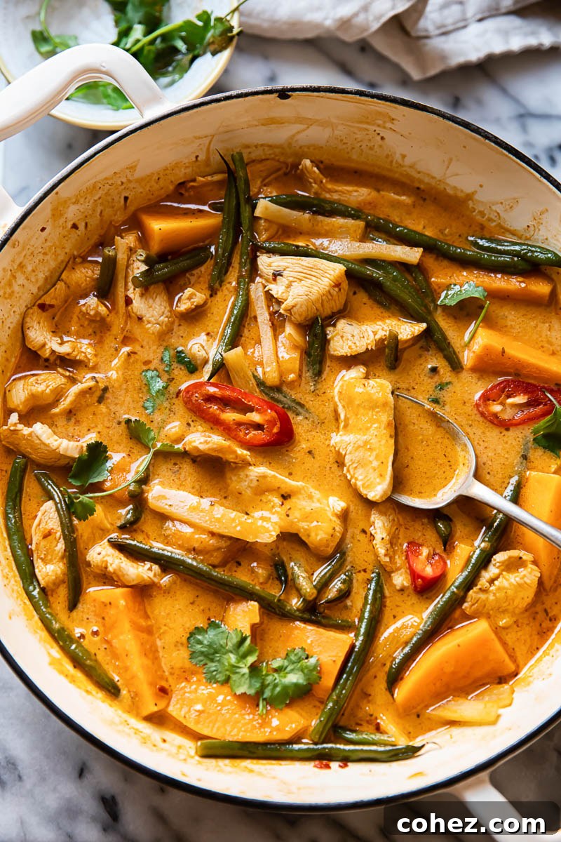 Golden Chicken and Sweet Potato Curry 2 A large white pan holds a generous portion of vibrant Thai red curry with chicken, sweet potatoes, and green beans, ready to be served.