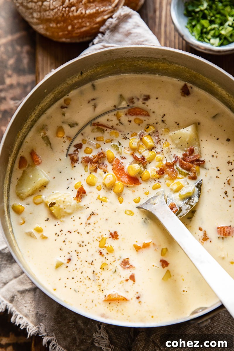 A top-down view of a generously filled pot of creamy corn chowder with sweet potatoes, garnished with fresh herbs, and a ladle resting inside, ready for serving.