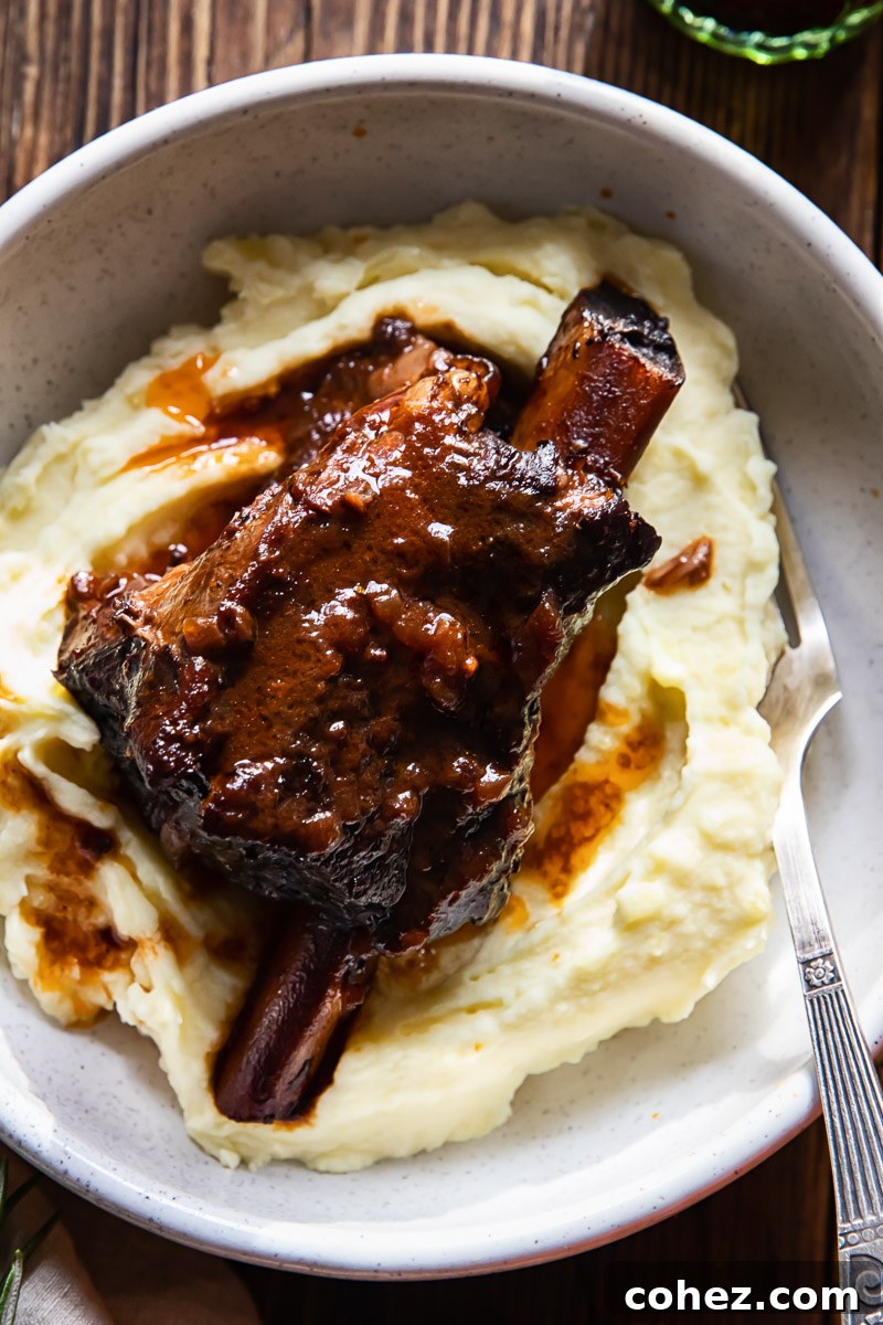 braised beef short rib in red wine sauce on top of creamy mashed potatoes in a bowl, garnished with fresh herbs
