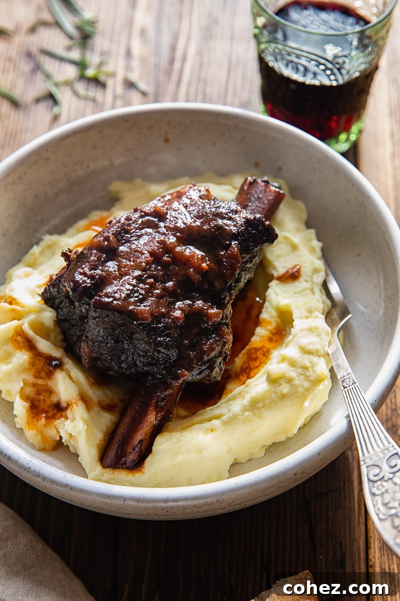 braised short rib on mashed potatoes in a bowl, with a glass of red wine and fresh rosemary garnish