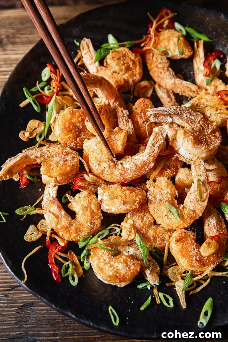 top down view of salt and pepper prawns on a dark platter, one shrimp being picked up by chopsticks
