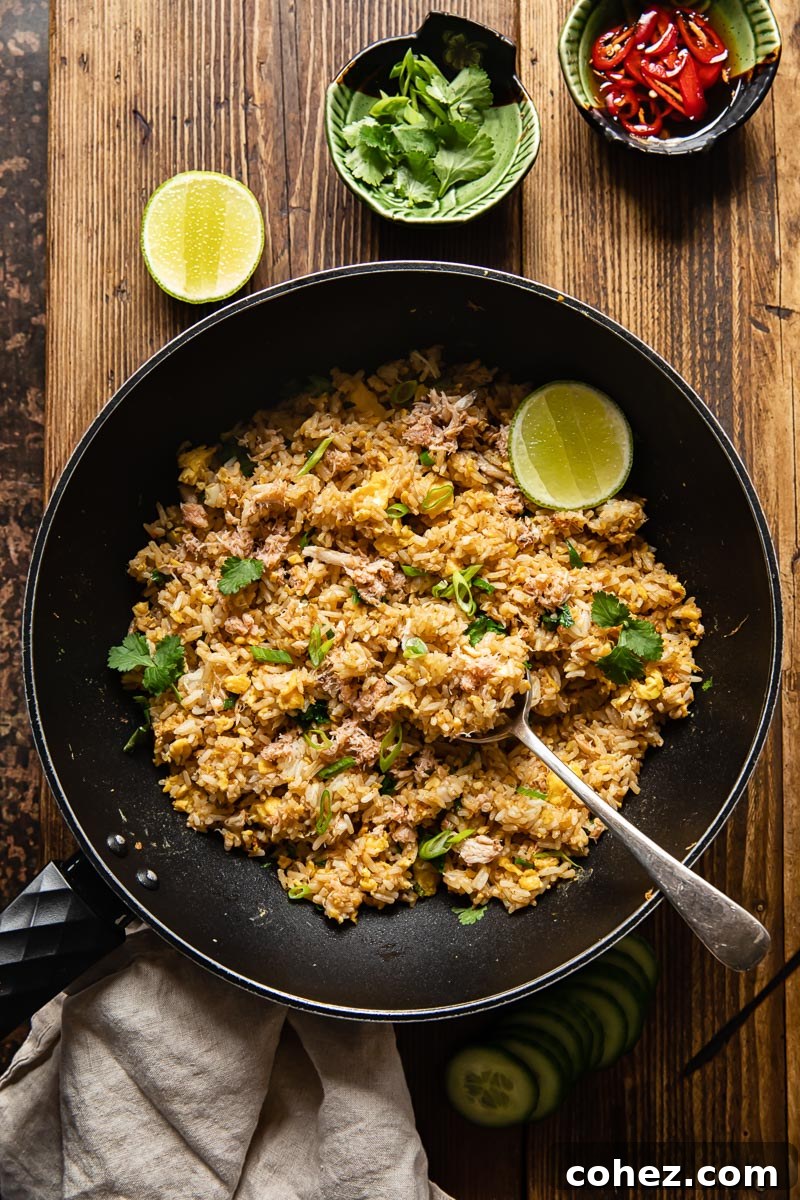 top down view of fried rice in a wok, a green bowl with greens and a green bowl with sliced red chilli next to the wok