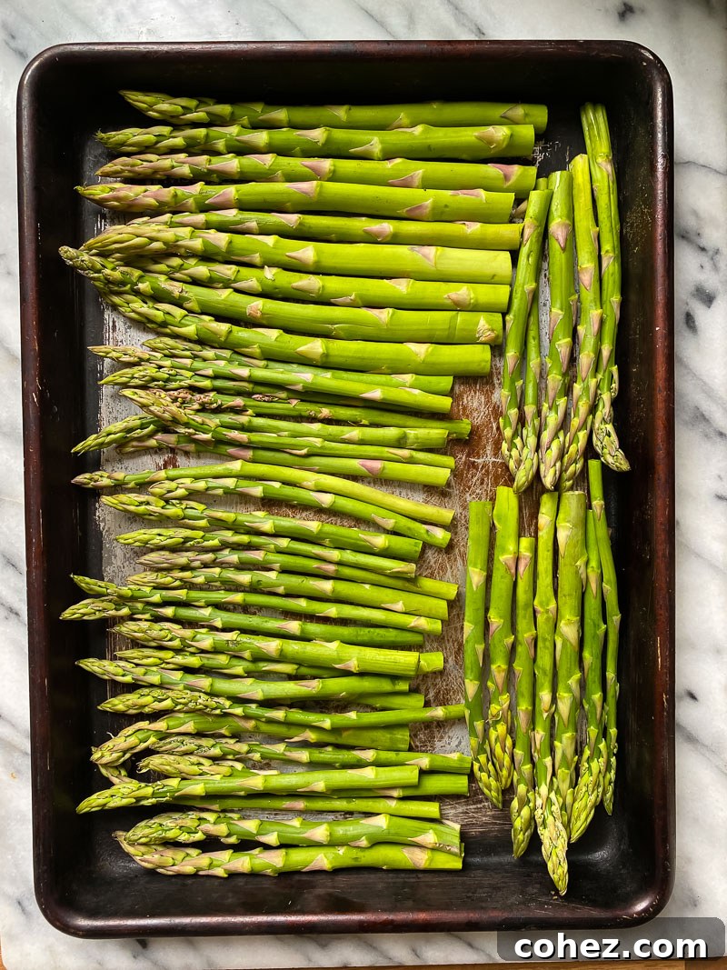 Fresh asparagus spears arranged on a baking sheet, glistening with olive oil and salt, ready for roasting.