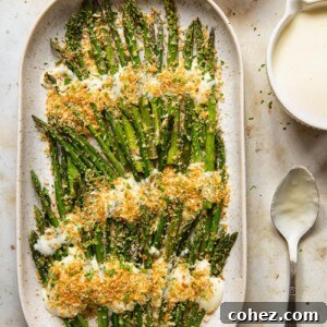 Close-up, top-down view of roasted asparagus spears generously coated in Mornay sauce and sprinkled with golden-brown herb and garlic breadcrumbs.