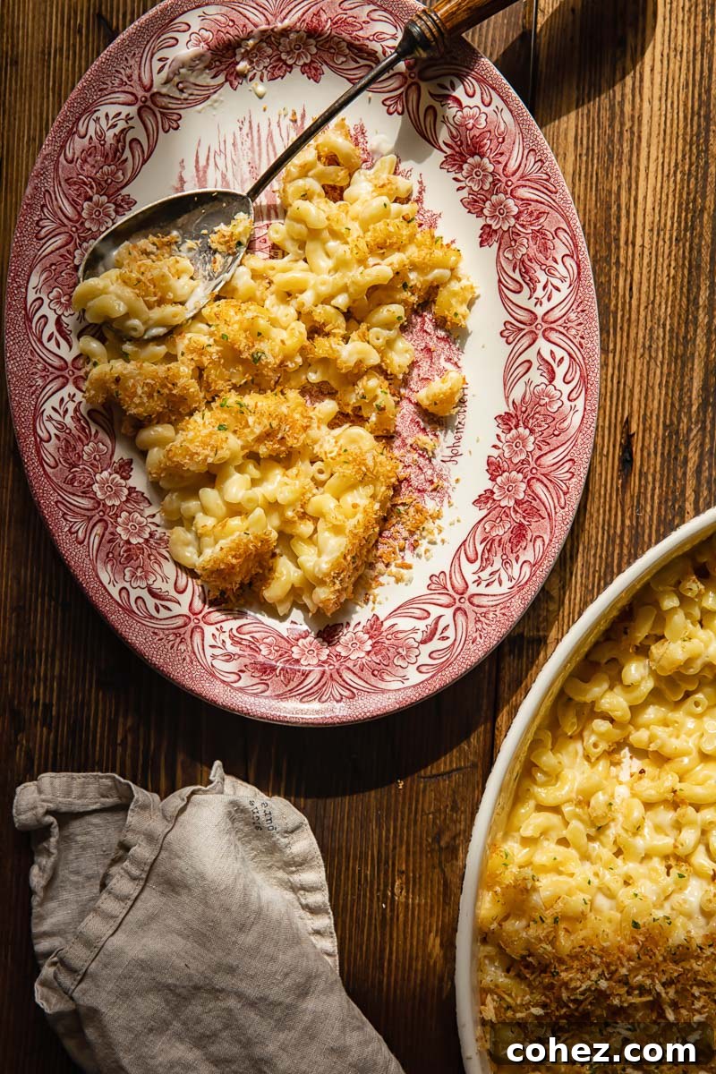 An appetizing close-up of a serving of baked macaroni and cheese on a plate, next to a casserole dish filled with more mac and cheese, resting on a cream-colored napkin.