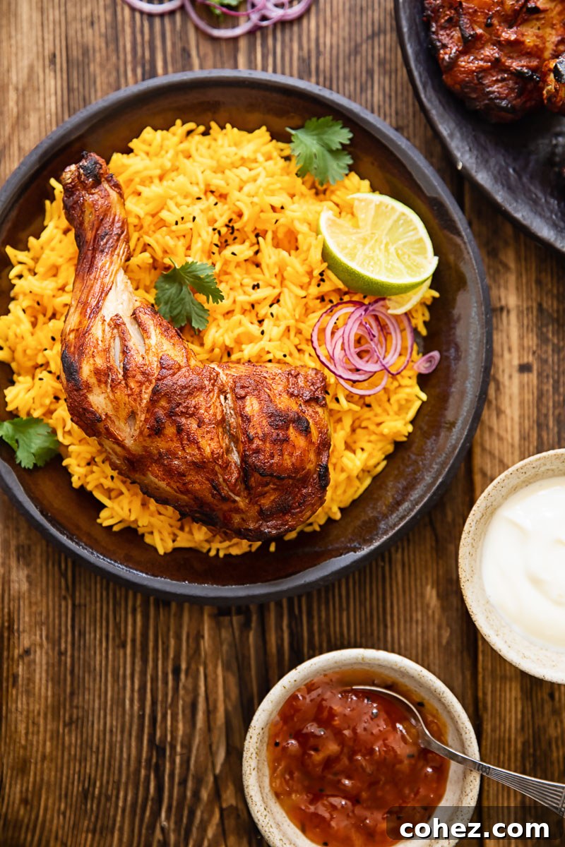 Tandoori chicken on yellow rice on a brown plate, with fresh cilantro and lime wedges around it