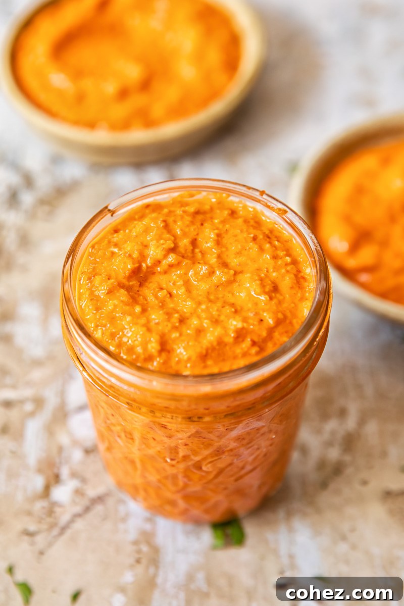 Close-up, top-down view of vibrant red Romesco sauce in a clear glass jar, showcasing its rich texture