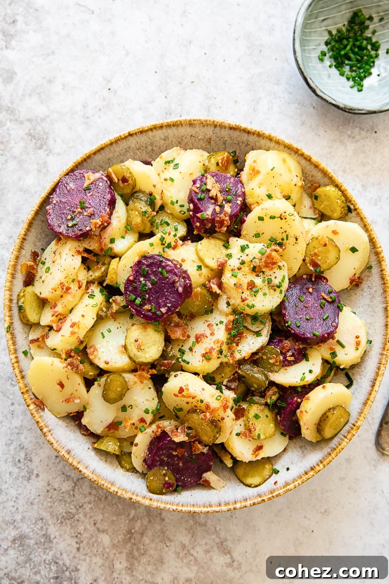 Hearty German Double Potato Salad with Crispy Bacon and Zesty Chive Vinaigrette 2 Top-down view of vibrant German potato salad with white and purple potatoes, garnished with fresh chives