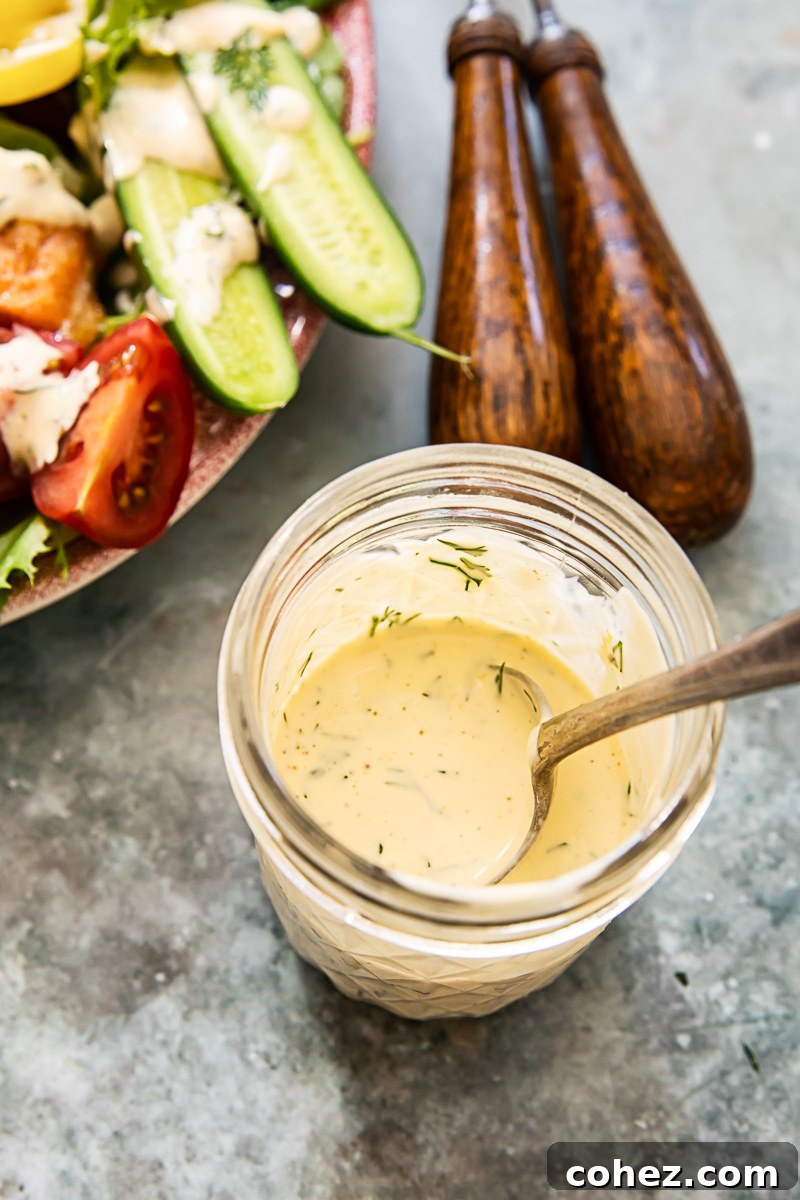 Homemade lemon dill dressing in a clear mason jar, highlighting its creamy texture and fresh herbs, ready to be poured over a vibrant salad.