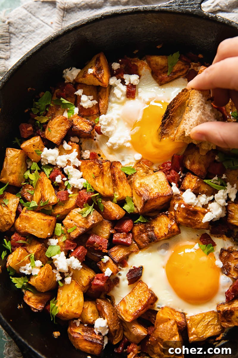 Spicy Chorizo Hash with Feta 3 a hand dipping bread into an egg yolk and cubed potatoes in a pan