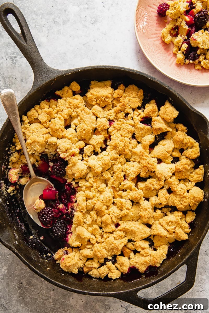 Top-down view of a golden-brown apple and blackberry crumble in a cast iron pan, ready to be served