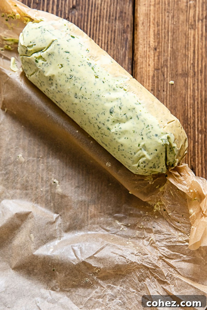 A log of freshly made garlic herb butter being carefully wrapped in parchment paper, showcasing the process of preparing it for chilling and future use.