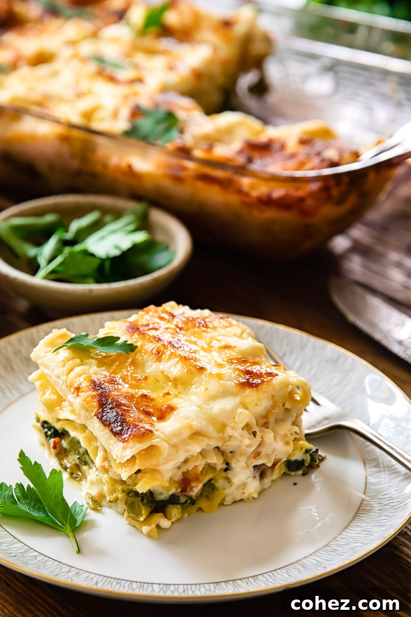 A slice of creamy white chicken lasagna on a plate, with a full pan of lasagna in the background, showcasing rich layers and golden-brown top.