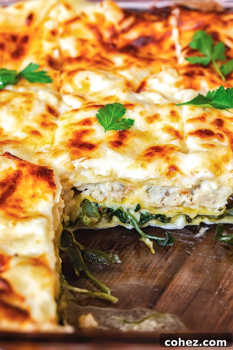 Close-up of a serving of white chicken lasagna, revealing the intricate layers of pasta, creamy sauce, chicken, and green vegetables.